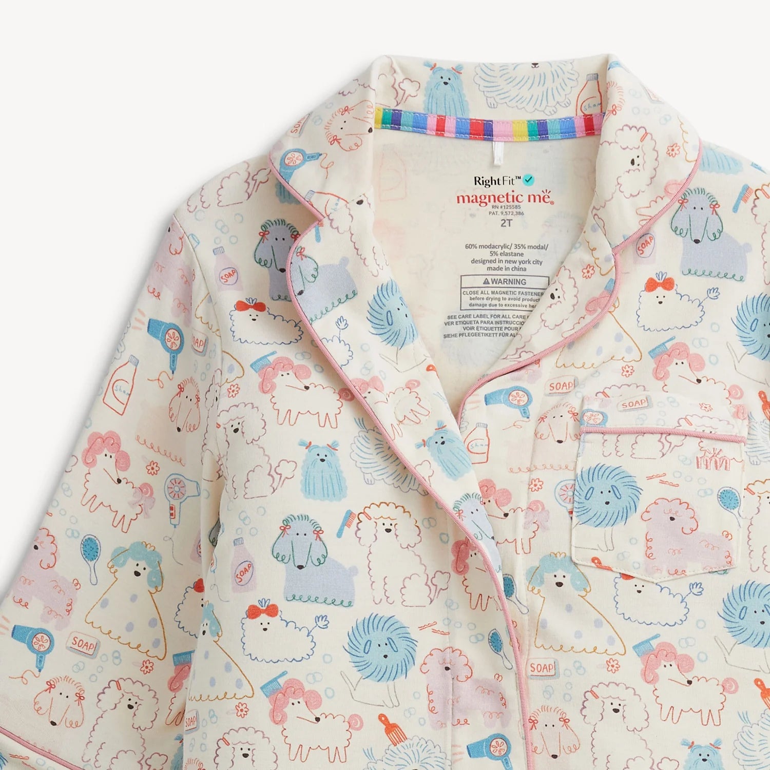 A close-up of a children's pajama top with a playful dog print. The pajamas feature a cream base color with cartoon dogs in light blue, pink, and orange, outlined in black.
