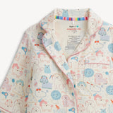 A close-up of a children's pajama top with a playful dog print. The pajamas feature a cream base color with cartoon dogs in light blue, pink, and orange, outlined in black.