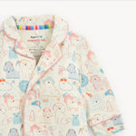 A close-up of a children's pajama top with a cute cartoon dog and grooming accessory print on a cream background, featuring pink piping and a visible inner neck label reading 'magnetic me'.