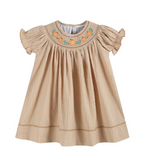 A beige baby girl's dress with vertical stripes, ruffled short sleeves, and a smocked neckline decorated with embroidered orange pumpkins and green leaves, shown on a plain white background.