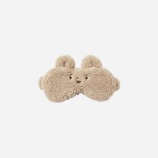 A pair of beige teddy-textured sleep masks shaped like a bear face, shown against a solid light gray background.