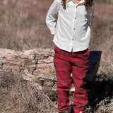 A child standing outdoors in a field wearing a white long-sleeve button-up shirt and red plaid pants.