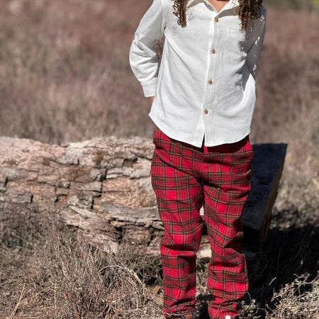A child standing outdoors in a field wearing a white long-sleeve button-up shirt and red plaid pants.
